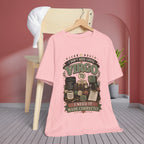 A light pink graphic t-shirt hanging on a wooden hanger from a wooden chair in a styled room setting. The shirt features a retro-style graphic with the text 'I DON'T NEED COFFEE VIRGO I NEED IT MADE CORRECTLY' and illustrations of coffee cups, books, and celestial elements.