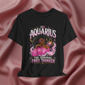 Black t-shirt with Aquarius design featuring a black woman and text 'The original free thinker' on a pink fabric background