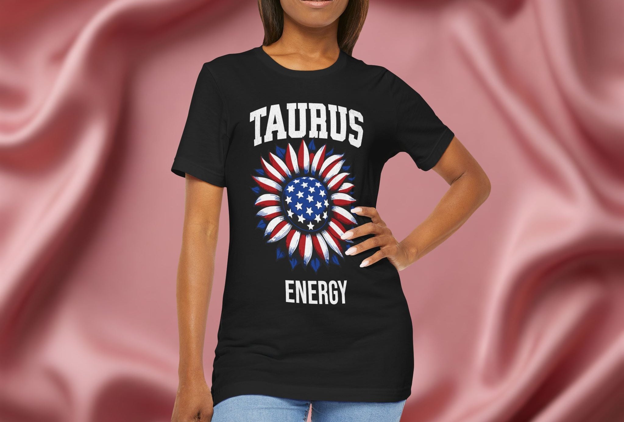 Person wearing a black t-shirt with American flag sunflower and 'TAURUS ENERGY' text on a textured pink background