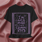 Black t-shirt with purple text 'I'm not a mess I'm a Gemini and graphics on a pink fabric background