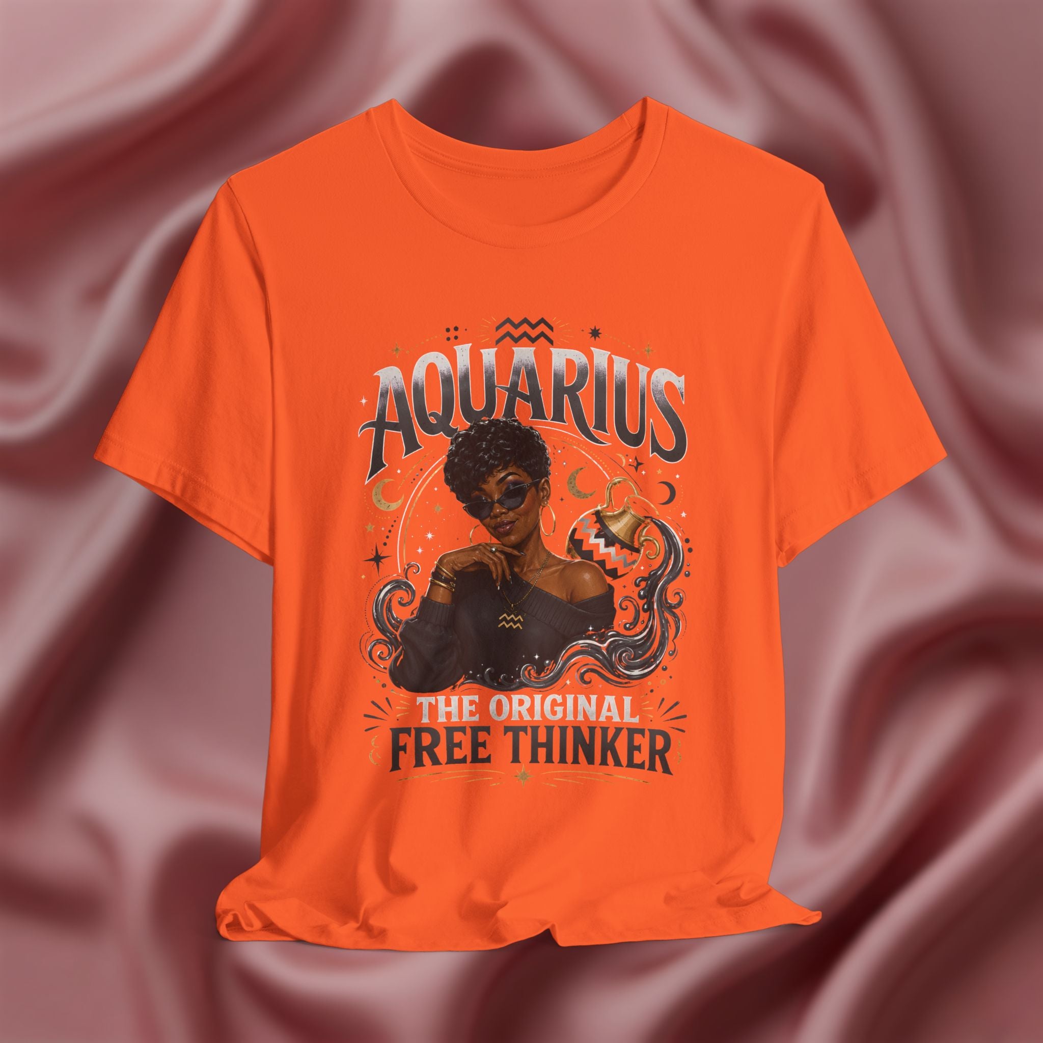 Orange t-shirt with Aquarius design featuring a black woman and text 'The original free thinker' on a pink fabric background