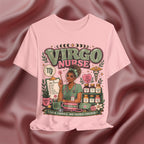 A light pink short-sleeve graphic T-shirt displayed against a draped satin fabric background. The shirt features a detailed 'Virgo Nurse' illustration with a nurse character, medical tools, books, and herbs, with the text 'VIRGO NURSE' and 'CALM, CAPABLE, AND DOUBLE-CHECKED.