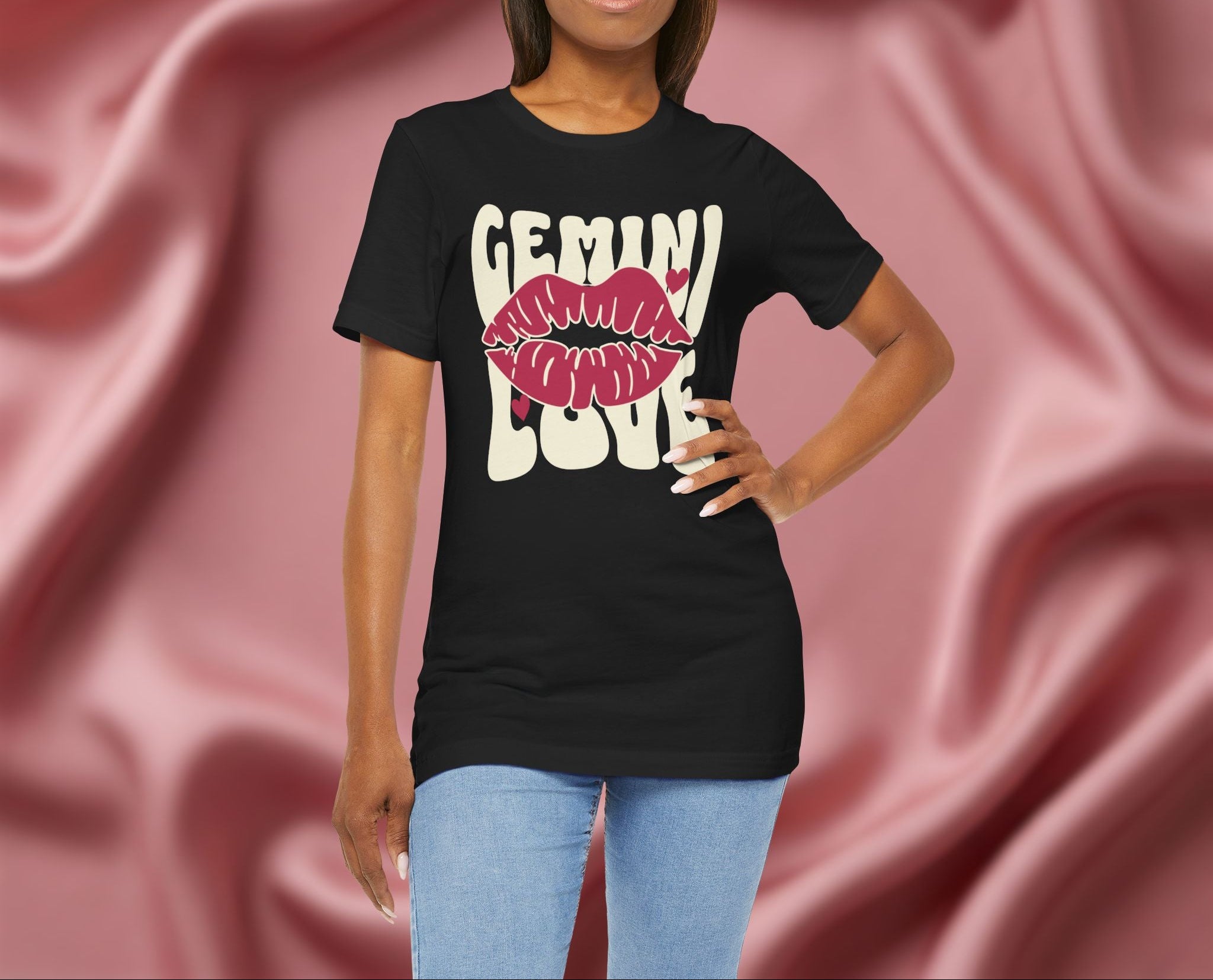 Woman wearing a black t-shirt with 'GEMINI Love' and lips design on a pink fabric background