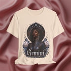 Soft cream T-shirt with a graphic design of a woman, flowers, and the word 'Gemini' on a pink fabric background.