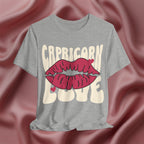 Gray t-shirt with 'Capricorn Love'  with hearts and lips graphic on a pink fabric background