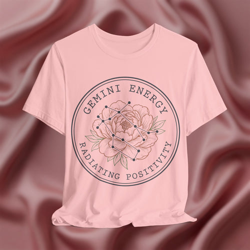 Pink t-shirt with 'Gemini Energy Radiating Positivity' design on a maroon fabric background