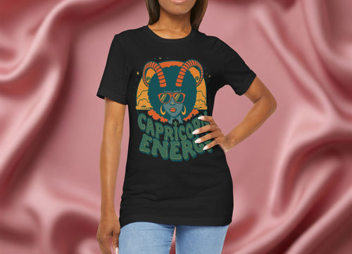 Woman wearing a black t-shirt with 'Capricorn Energy' design against a pink fabric background