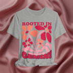 Gray t-shirt with red and orange floral design and 'Rooted in Gemini' text on a pink fabric background