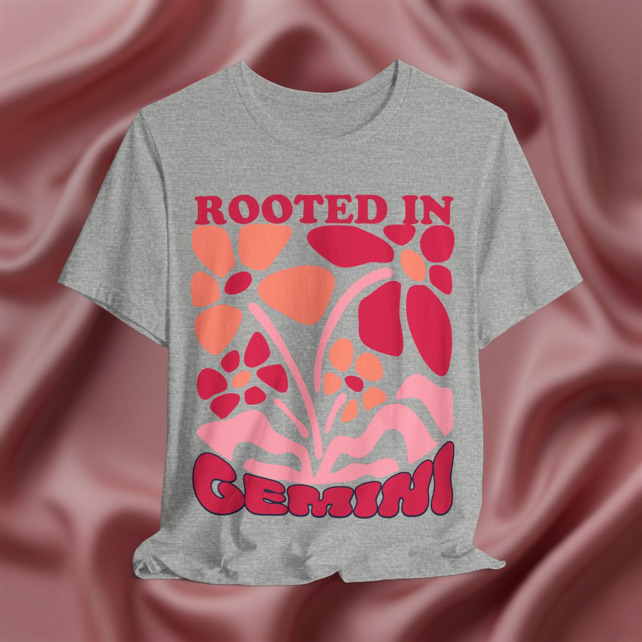 Gray t-shirt with red and orange floral design and 'Rooted in Gemini' text on a pink fabric background