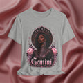 Gray t-shirt with a graphic design of a woman, flowers, and the word 'Gemini' on a pink fabric background.