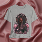 Gray t-shirt with a graphic design of a woman, flowers, and the word 'Gemini' on a pink fabric background.