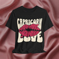 Black t-shirt with 'Capricorn Love'  with hearts and lips graphic on a pink fabric background