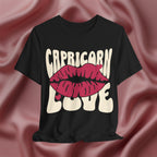 Black t-shirt with 'Capricorn Love'  with hearts and lips graphic on a pink fabric background