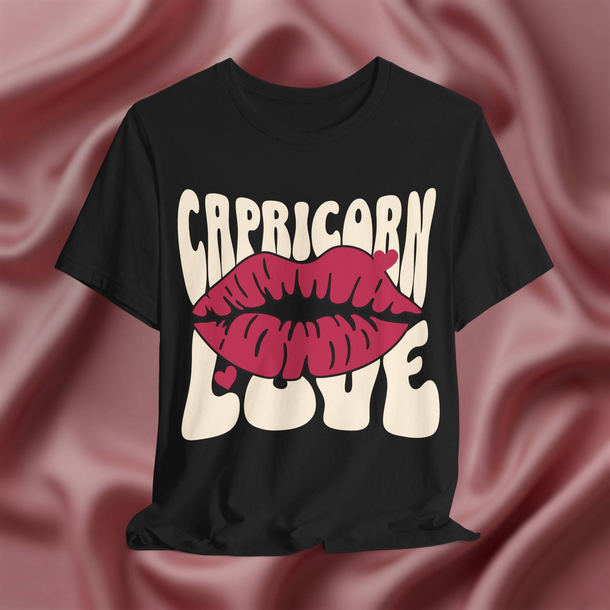 Black t-shirt with 'Capricorn Love'  with hearts and lips graphic on a pink fabric background