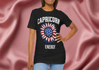 Person wearing a black t-shirt with American flag sunflower and 'CAPRICORN ENERGY' text on a textured pink background