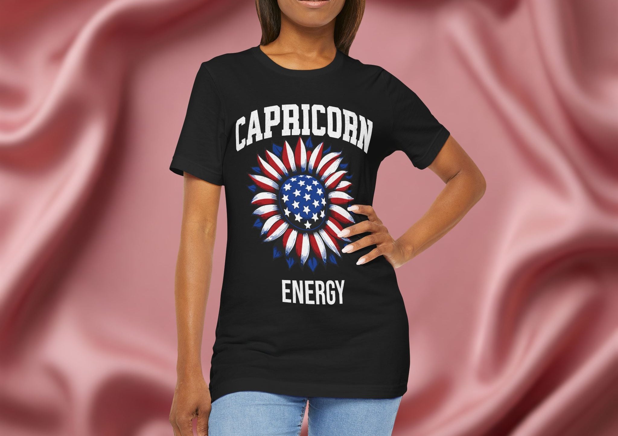 Person wearing a black t-shirt with American flag sunflower and 'CAPRICORN ENERGY' text on a textured pink background