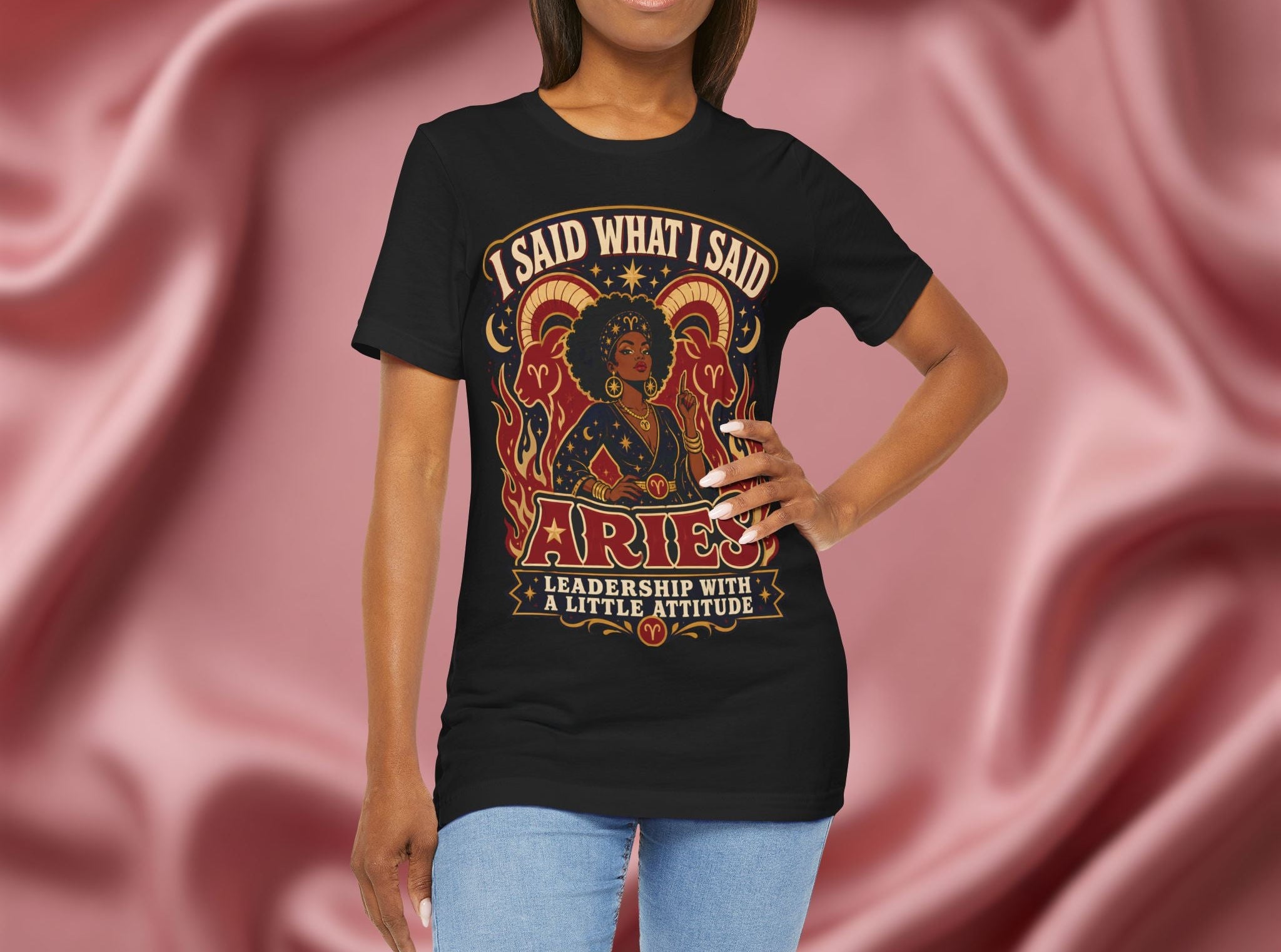 Person wearing a black t-shirt with Aries zodiac design on a pink fabric background