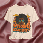 An off-white short-sleeve t-shirt with a retro graphic of a Black woman with an afro, sunglasses, and the text 'VIRGO ENERGY' in orange and teal, displayed against a draped dusty rose satin background.