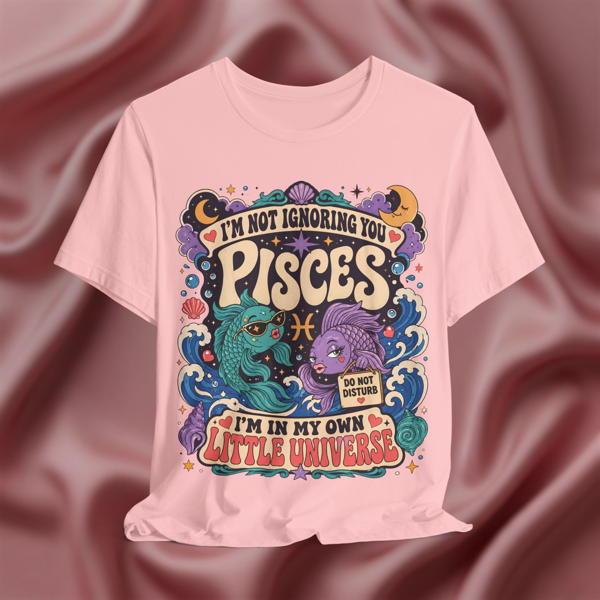 Pink t-shirt with Pisces zodiac design on a maroon fabric background