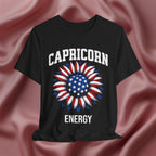 Black t-shirt with American flag sunflower and 'CAPRICORN ENERGY' text on a textured pink background