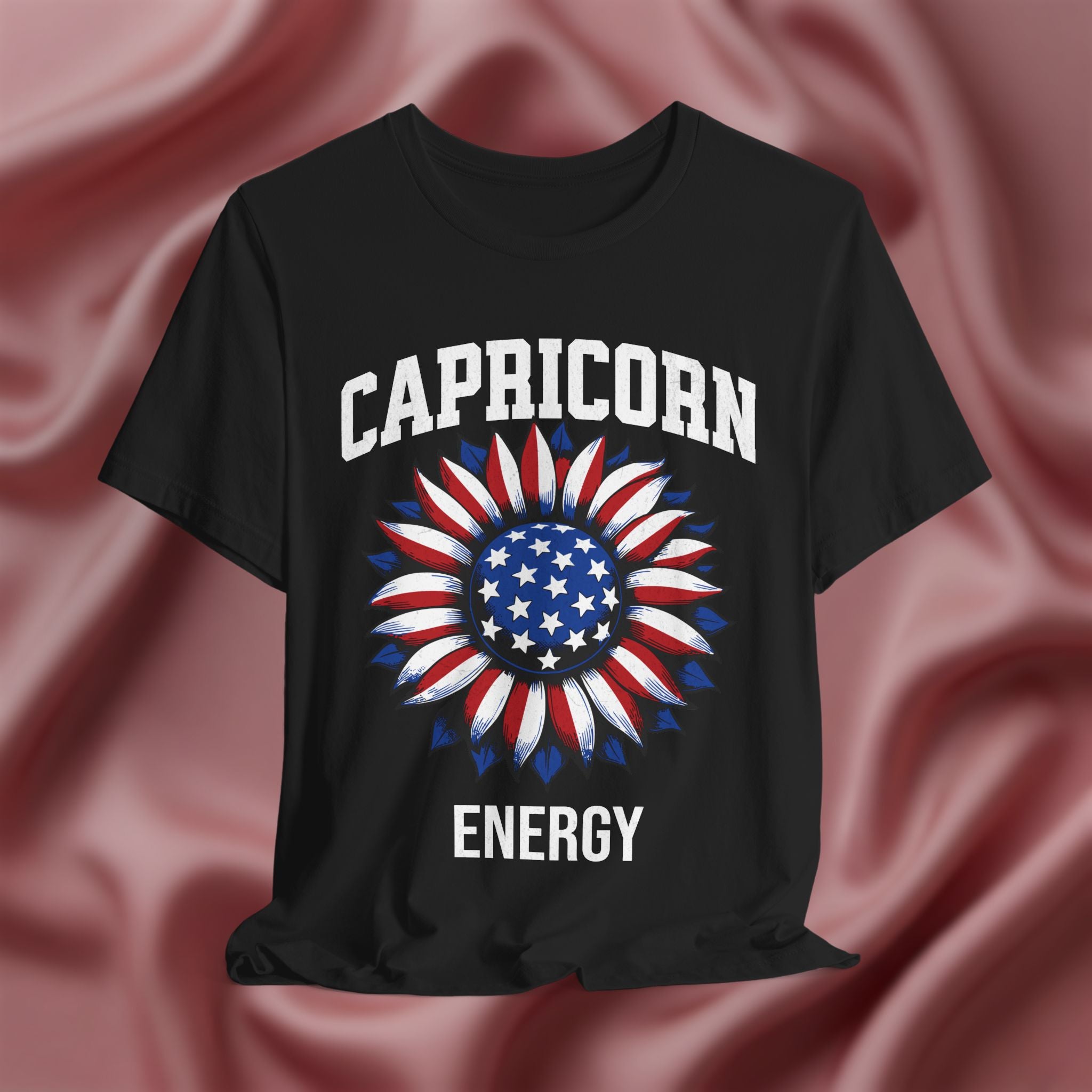 Black t-shirt with American flag sunflower and 'CAPRICORN ENERGY' text on a textured pink background