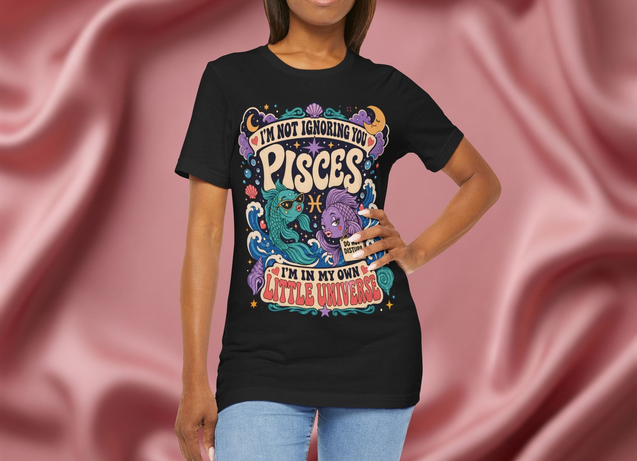 Person wearing a black t-shirt with colorful graphics and text against a pink fabric background
