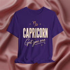 Purple t-shirt with 'Capricorn Get you one' text on a pink fabric background
