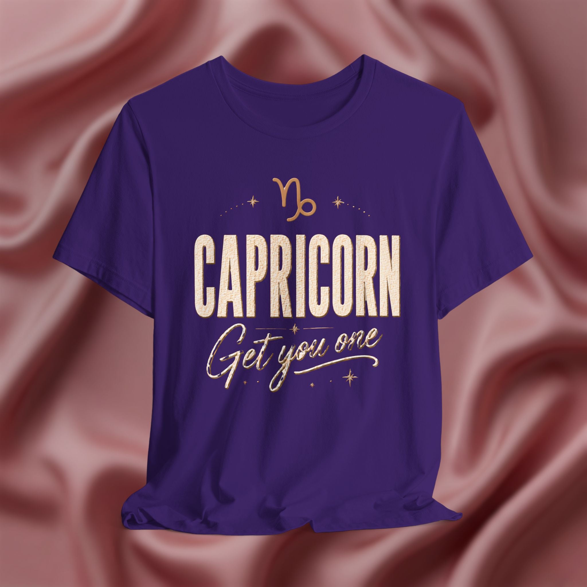 Purple t-shirt with 'Capricorn Get you one' text on a pink fabric background