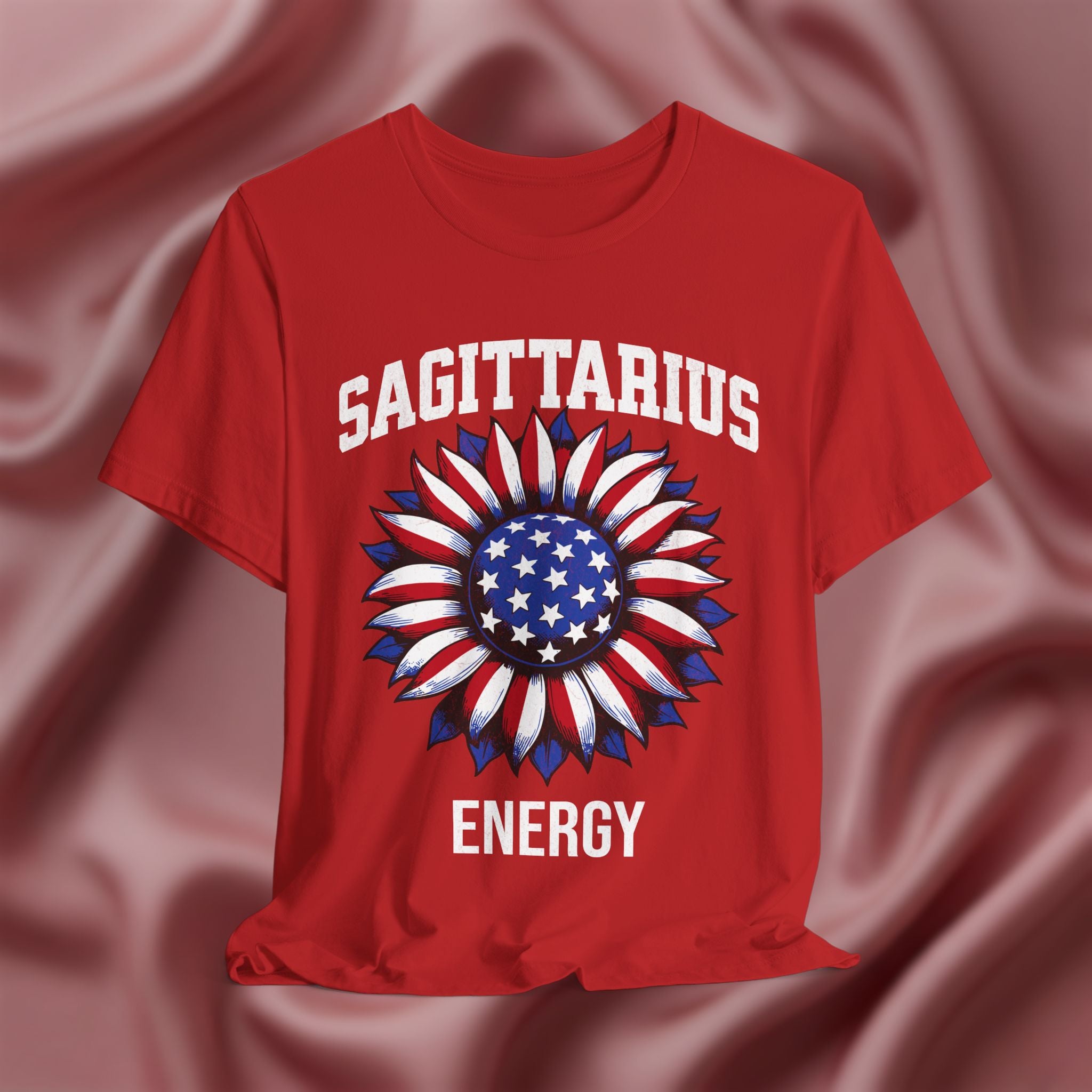 Red t-shirt with American flag sunflower and 'SAGITTARIUS ENERGY' text on a textured pink background
