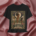 A black short-sleeve graphic t-shirt featuring an ornate vintage-style illustration of 'The Maiden Virgo' with celestial motifs, set against a draped dusty rose satin background.