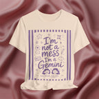 Soft cream t-shirt with purple text 'I'm not a mess I'm a Gemini and graphics on a pink fabric background