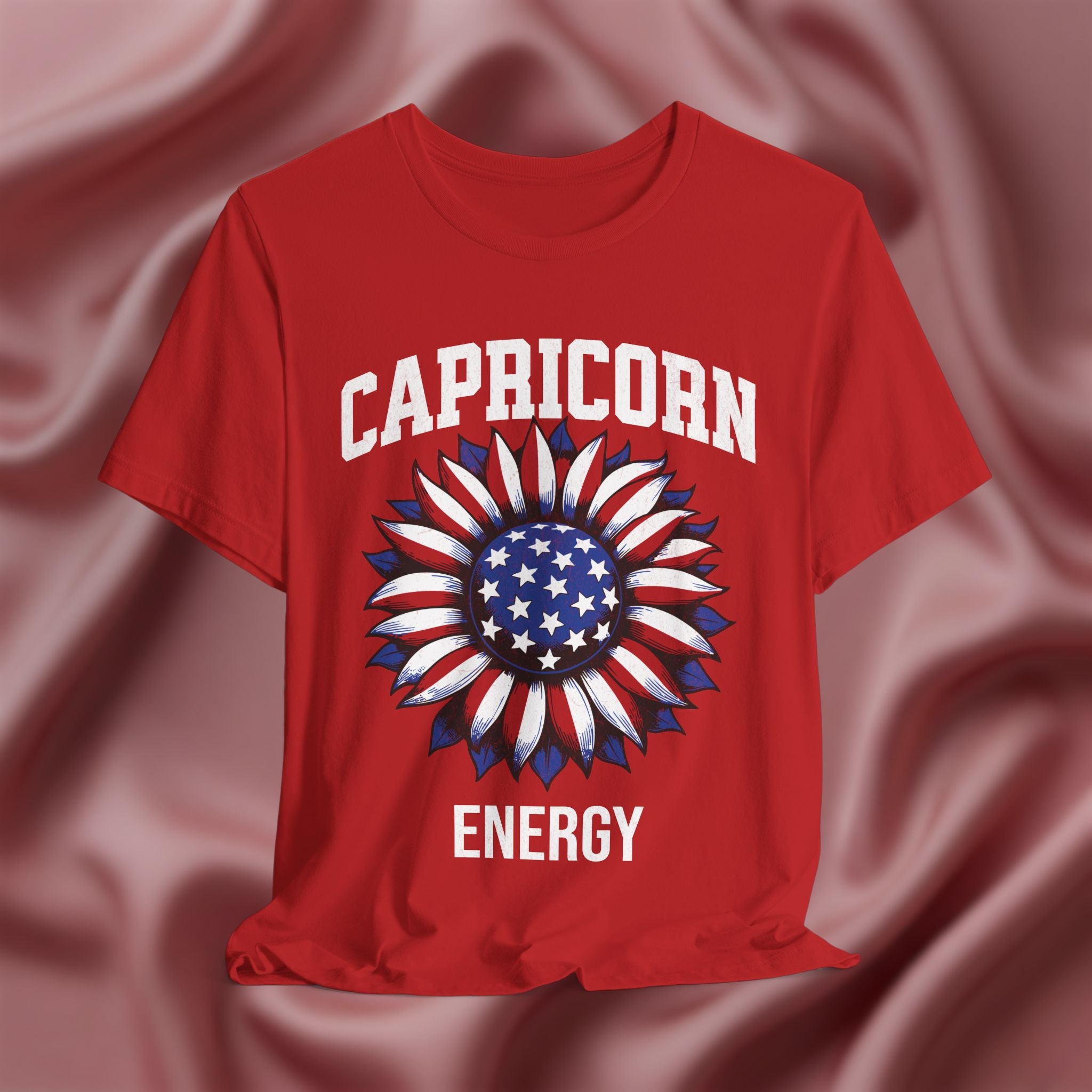 Red t-shirt with American flag sunflower and 'CAPRICORN ENERGY' text on a textured pink background