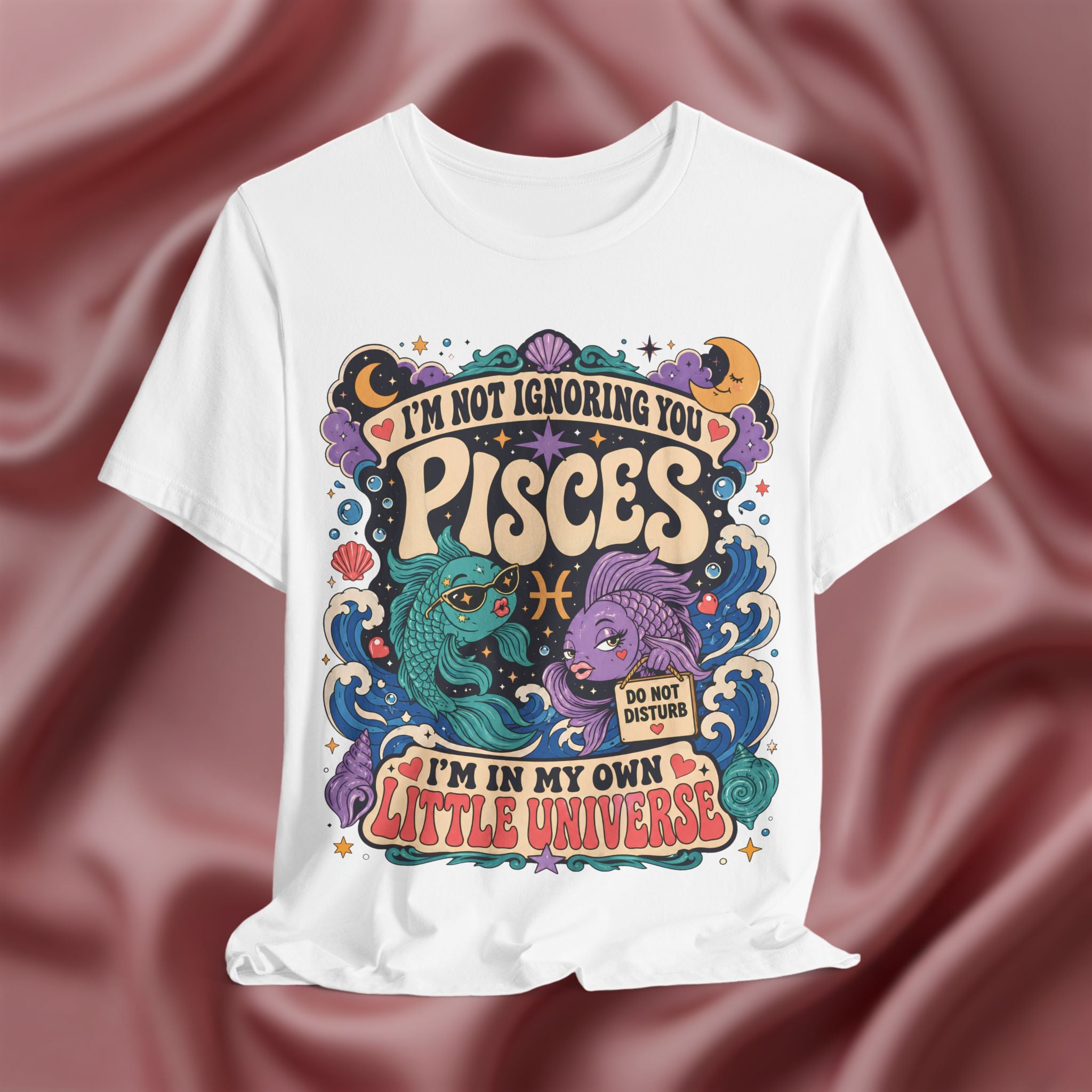 White t-shirt with Pisces zodiac design on a maroon fabric background