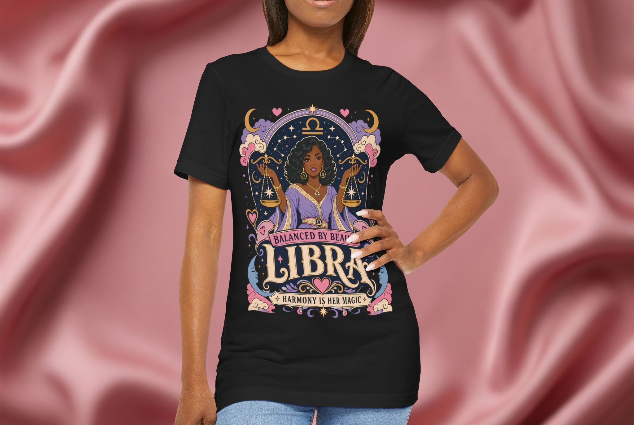 Woman wearing a black t-shirt with Libra zodiac design against a pink fabric background