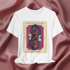 Sophisticated Queen Gemini Energy  White t-shirt with a graphic design of a woman holding coffee cups on a pink fabric background