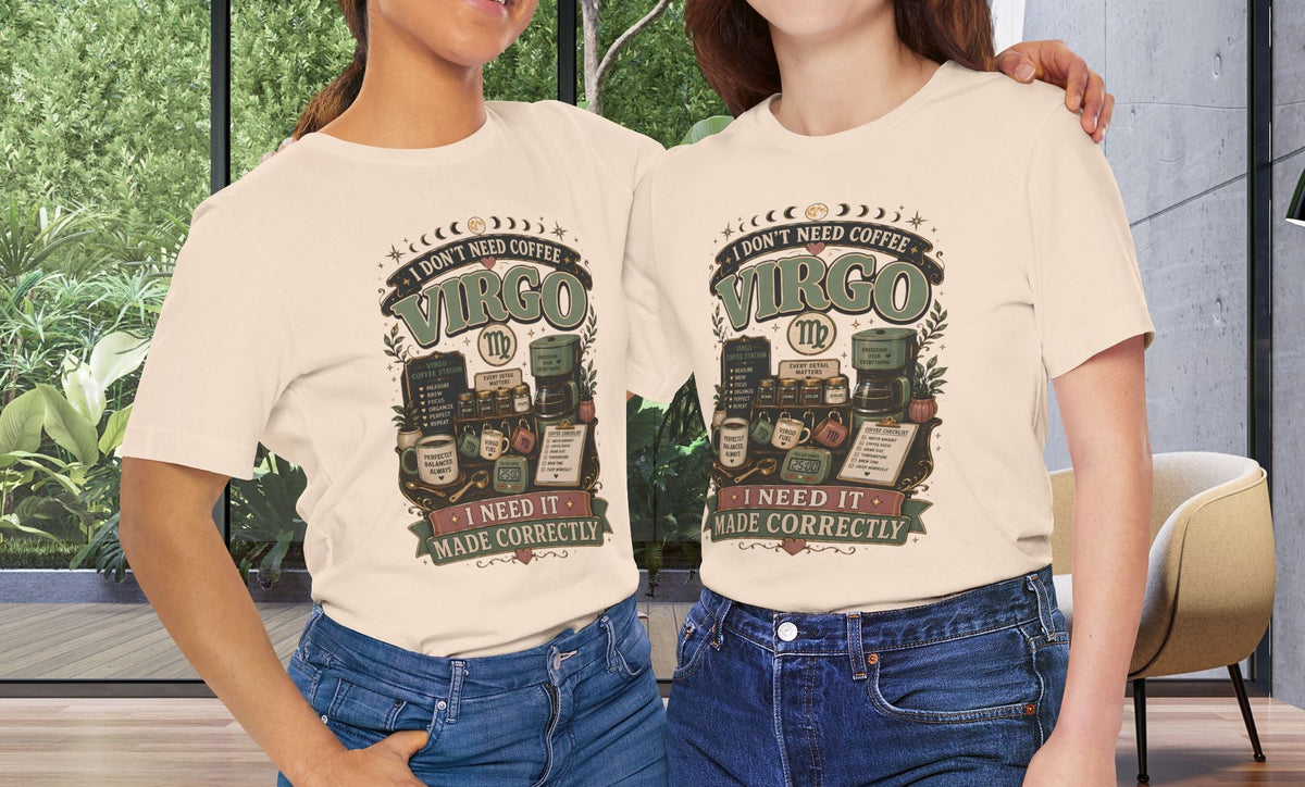 Two women standing indoors wearing matching cream graphic T-shirts with a vintage-style Virgo design and blue jeans, posed in front of large windows with greenery outside.