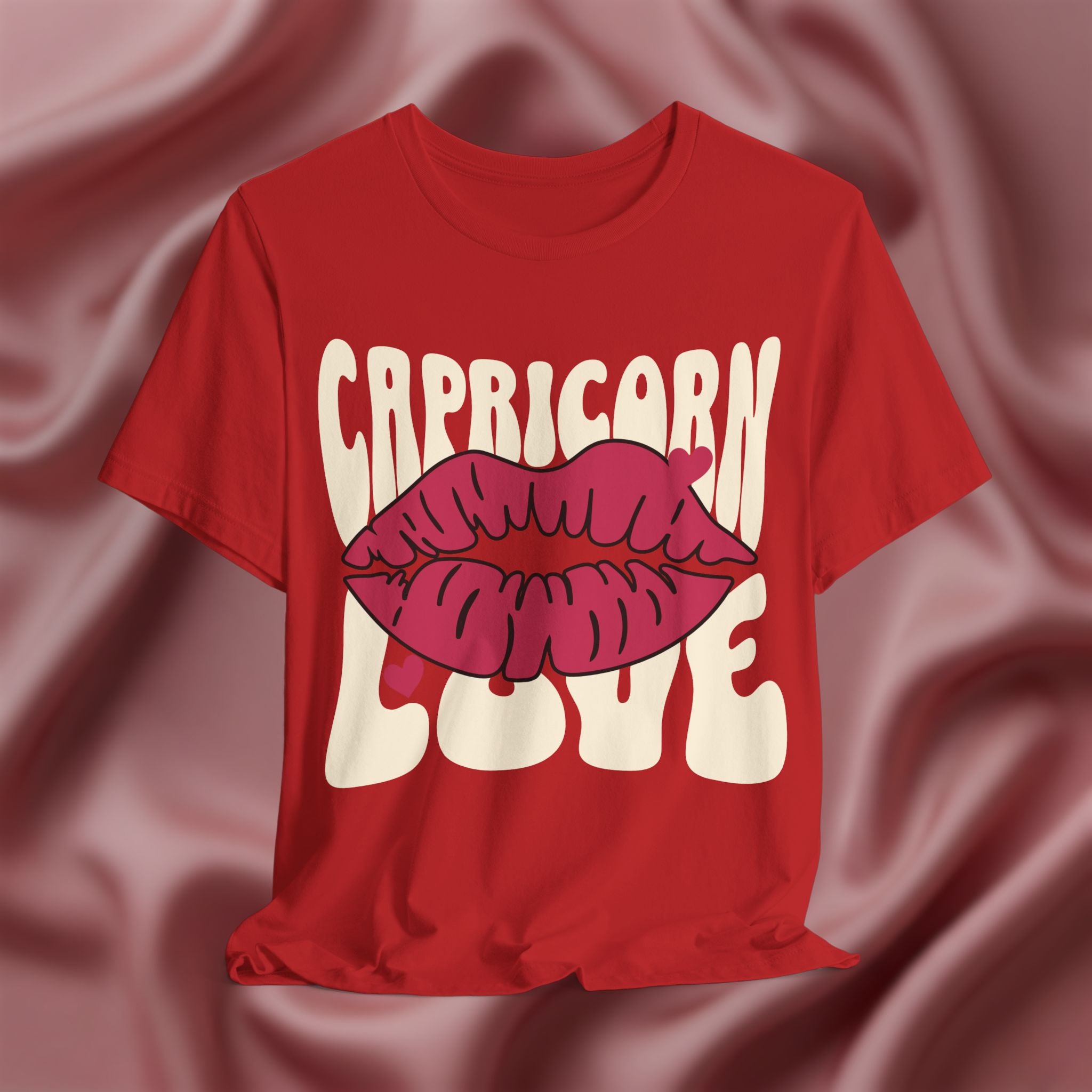 Red t-shirt with 'Capricorn Love'  with hearts and lips graphic on a pink fabric background