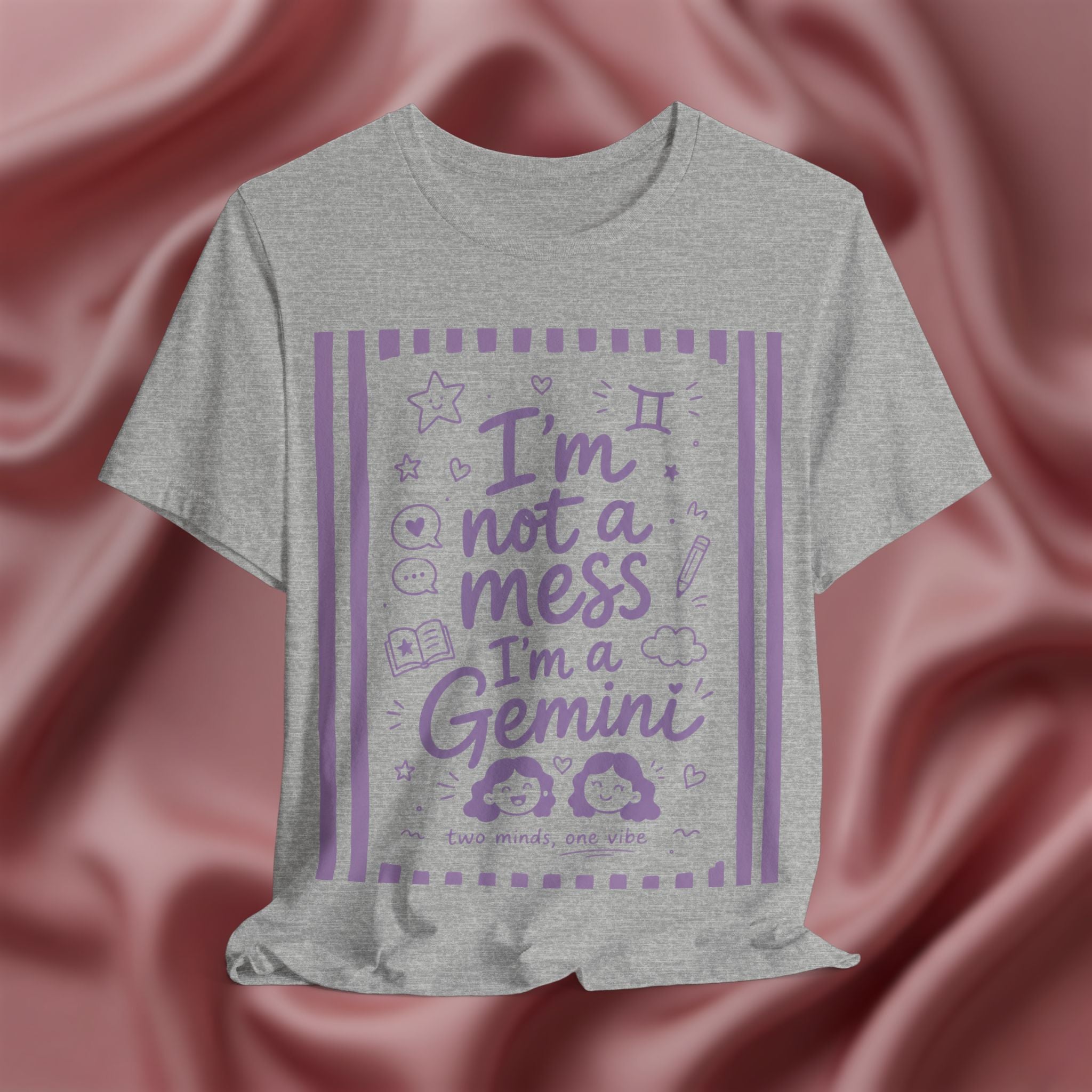 Gray t-shirt with purple text 'I'm not a mess I'm a Gemini and graphics on a pink fabric background