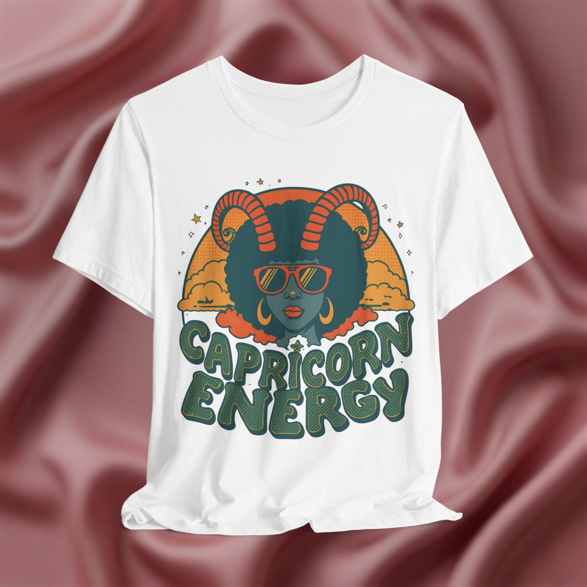 White t-shirt with Capricorn design and text on a maroon fabric background