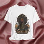 White t-shirt with 'Gemini' design featuring a black woman, roses, and astrological symbols on a maroon fabric background.