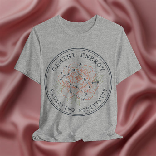 Gray t-shirt with 'Gemini Energy Radiating Positivity' design on a pink fabric background