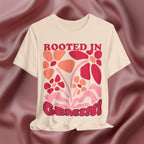 Soft cream t-shirt with floral design and text 'Rooted in Genius' on a maroon fabric background
