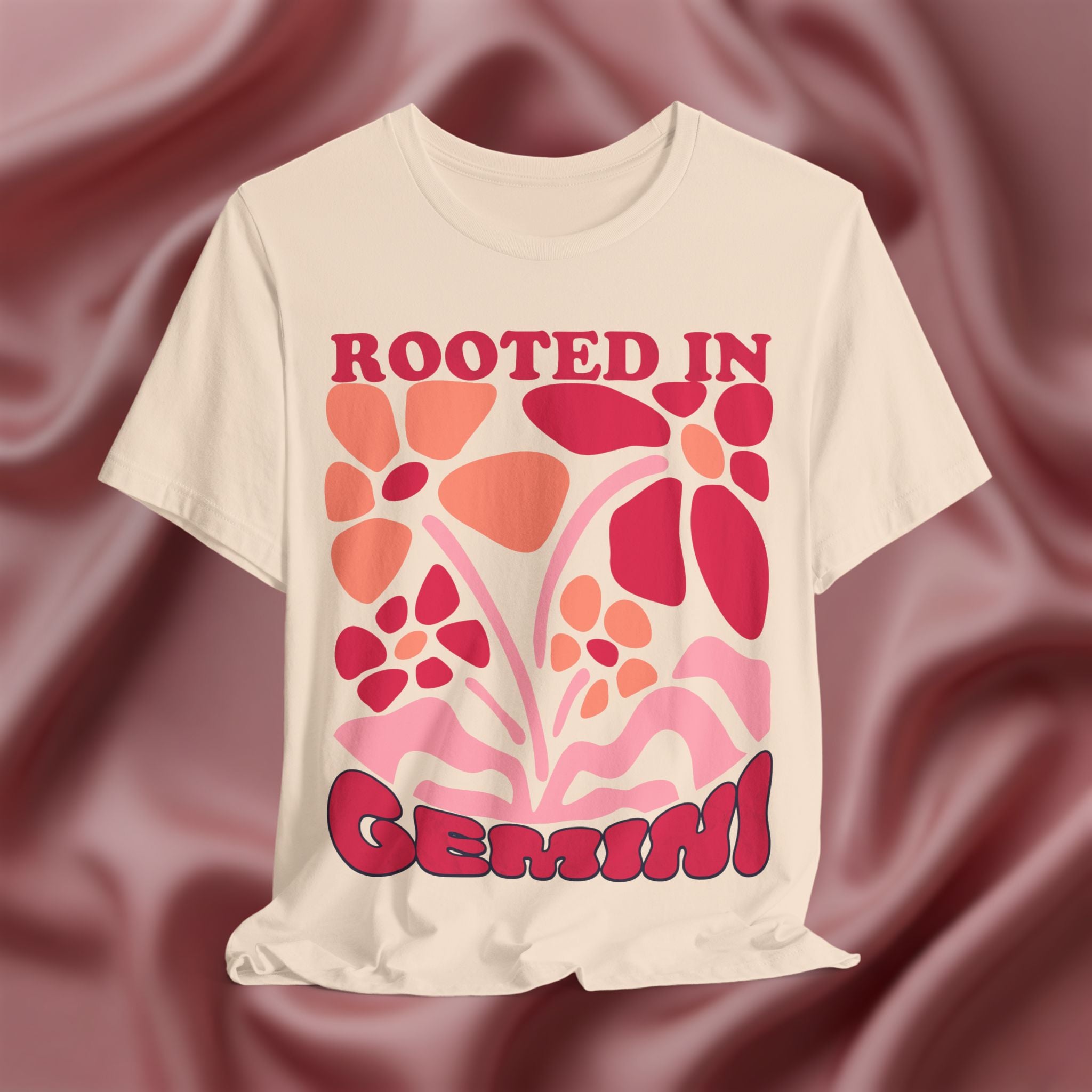 Soft cream t-shirt with floral design and text 'Rooted in Genius' on a maroon fabric background