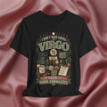 A black short-sleeve graphic T-shirt displayed against a draped dusty rose satin fabric background. The shirt features a vintage-style astrological graphic for Virgo with the text 'I DON'T NEED COFFEE VIRGO I NEED IT MADE CORRECTLY' and illustrations of old apothecary bottles, jars, and scrolls.