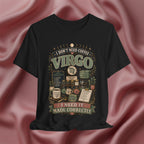 A black short-sleeve graphic T-shirt displayed against a draped dusty rose satin fabric background. The shirt features a vintage-style astrological graphic for Virgo with the text 'I DON'T NEED COFFEE VIRGO I NEED IT MADE CORRECTLY' and illustrations of old apothecary bottles, jars, and scrolls.