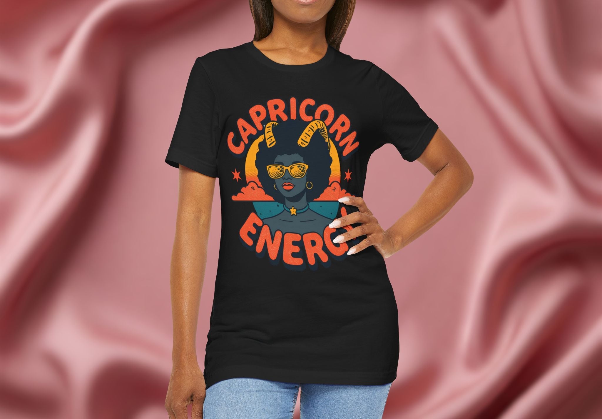 Woman wearing a black t-shirt with 'Capricorn Energy' design against a pink fabric background
