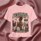 A pink graphic t-shirt featuring a detailed illustration of a Virgo stylist surrounded by hair tools and products, with the text 'VIRGO STYLIST' and 'PRECISION IS THE WHOLE VIBE'. The t-shirt is displayed against a draped, satin-like dusty rose background.