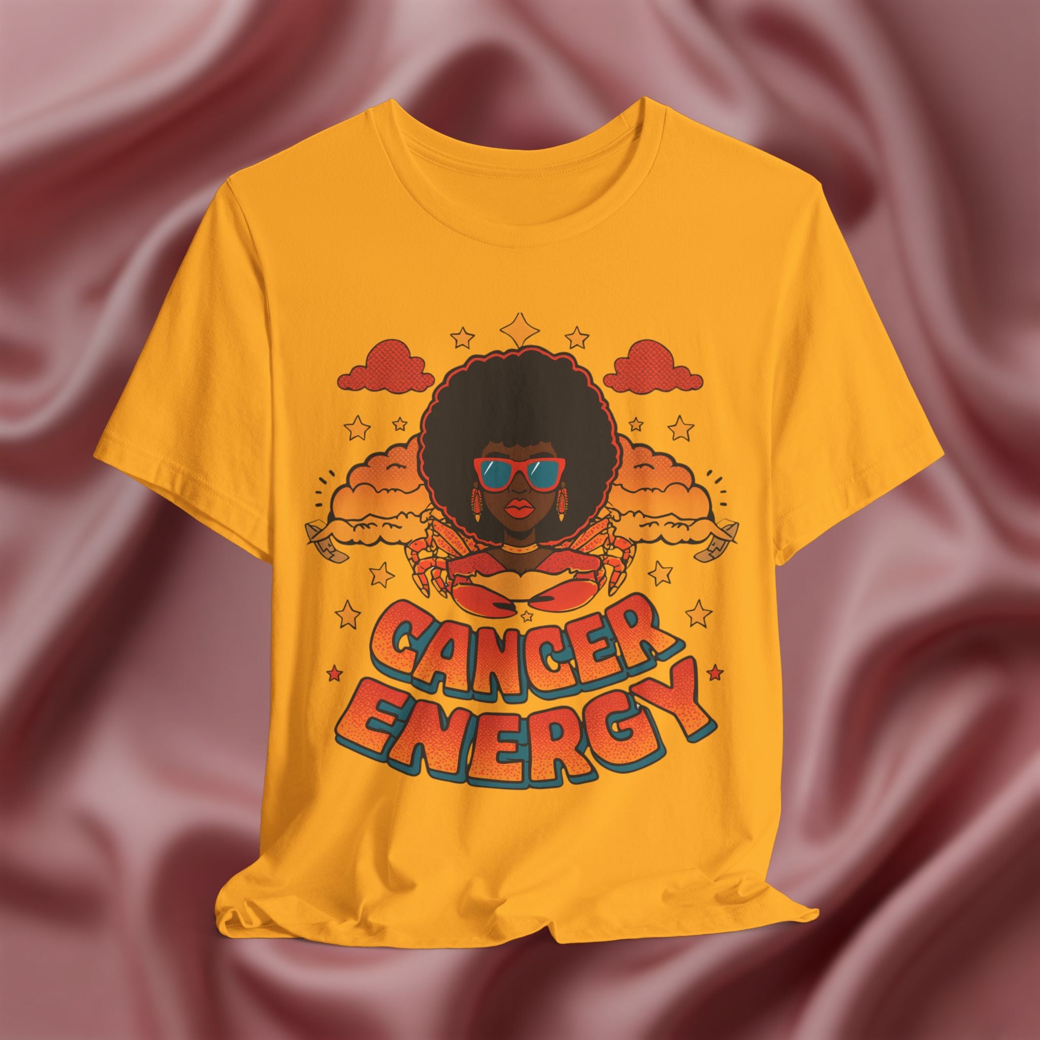 Gold Yellow t-shirt with a graphic design of a person with an afro and 'Cancer Energy' text on a pink fabric background.