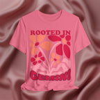 Pink t-shirt with floral design and text 'Rooted in Gemini' on a textured brown background