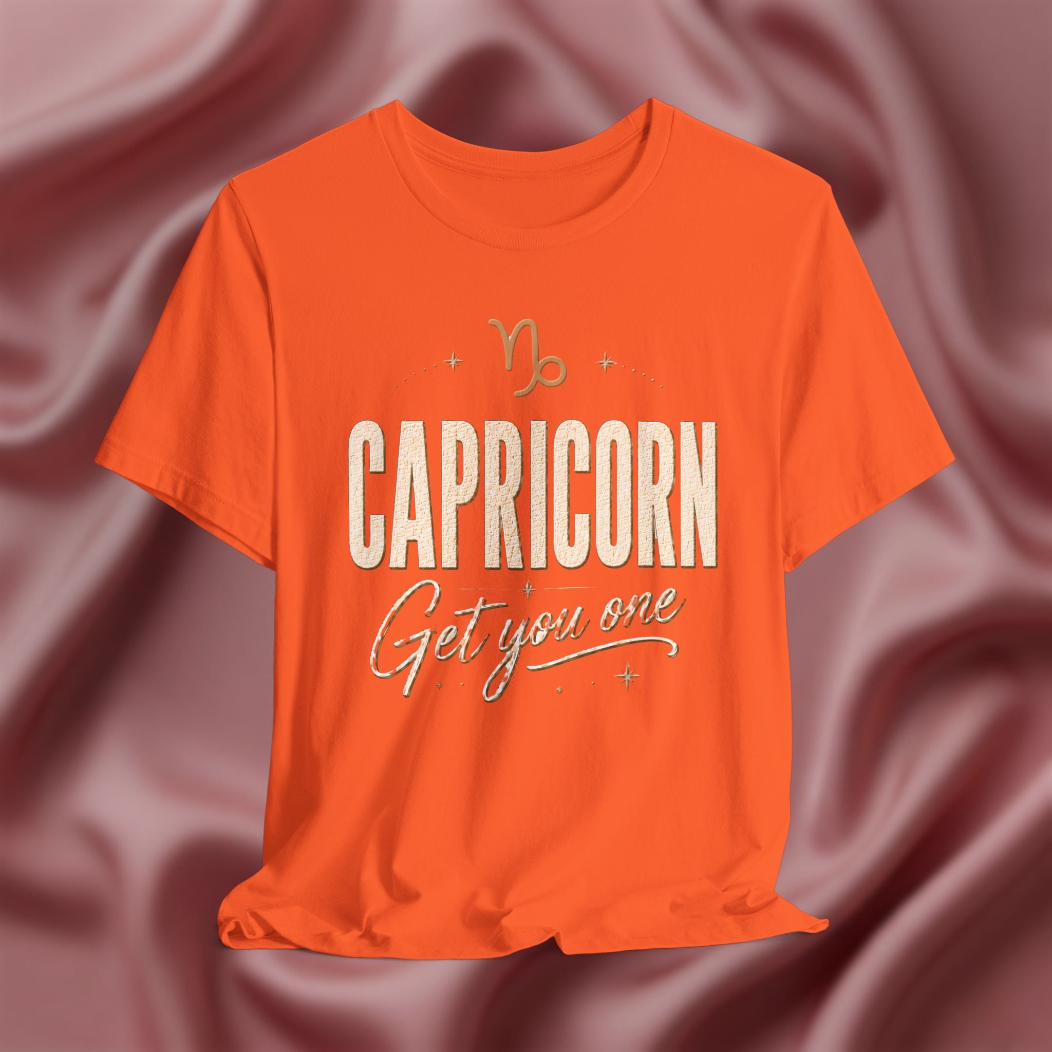 Orange t-shirt with 'Capricorn Get you one' text on a pink fabric background